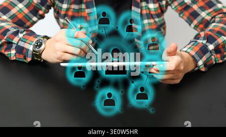 Futuristic human resources and social network concept. Businessman using tablet with glowing digital interface showing interconnected people icons. Gl Stock Photo