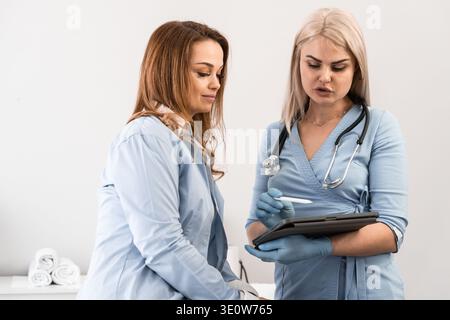 Confident female doctors collaborate while reviewing medical data on a tablet in a bright hospital office. Modern technology and teamwork drive effective patient care solutions Stock Photo