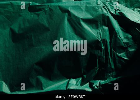 Dark green crumpled tissue paper texture with moody shadows. Abstract background, wrinkled emerald paper, dramatic lighting, organic folds, and minima Stock Photo