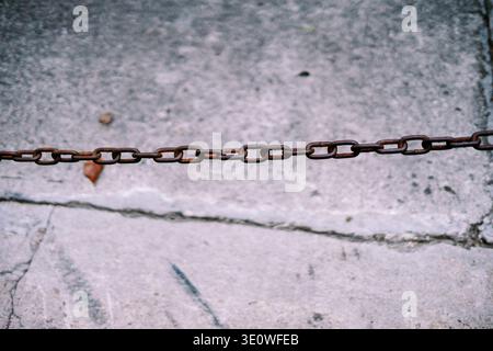 Close-up of a rusted metal chain against a textured, light grey concrete background. The old, corroded links create a strong visual barrier with shall Stock Photo