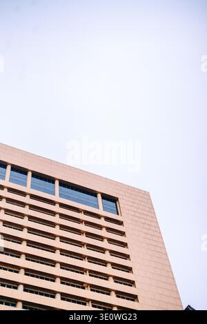 Low angle view of a modern high-rise building with a light-colored, panelled facade and dark windows, set against a clear, bright sky. Emphasizes cont Stock Photo