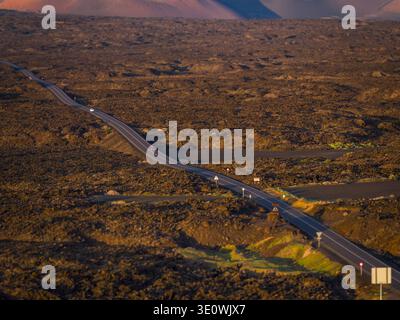 Aerial view of a ribbon of road stretches through the volcanic landscape, cutting a path through the dark, textured earth, Lanzarote, Canarias, Spain. Stock Photo