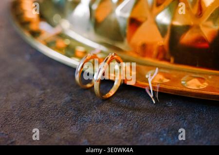 Two elegant golden wedding rings, one with a small diamond, rest on a dark, textured surface with a sparkling golden background. Perfect for themes of Stock Photo