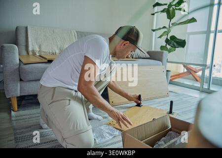 Man kneeling, assembling flat-pack furniture in his living room Stock Photo