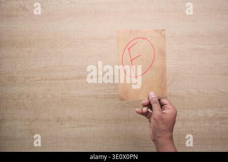 Hand holding card with letter F on brown background Stock Photo