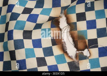 Checkered fabric with a burn mark showing damage Stock Photo