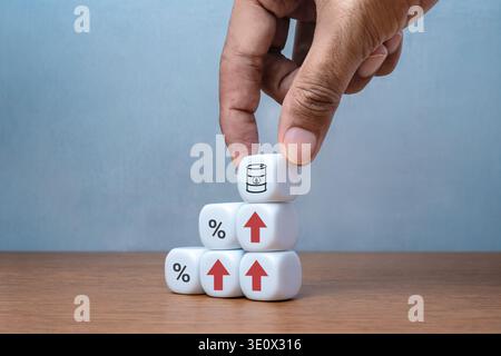 Hand placing cube with oil barrel icon on stacked blocks showing upward arrows and percent symbols. Rising oil prices, inflation, fuel cost increase Stock Photo