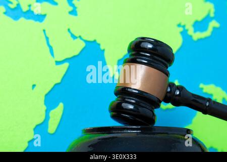 Black judge's gavel against a vibrant green and blue paper world map. International law, geopolitical conflict, global justice, and diplomatic rulings Stock Photo