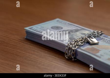A bundle of one hundred US dollar bills bound with a metal chain and secured with a padlock. Financial security, asset protection, frozen accounts Stock Photo
