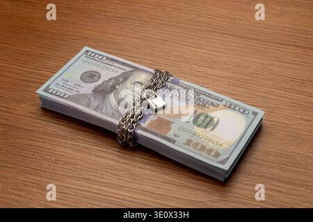 A bundle of one hundred US dollar bills bound with a metal chain and secured with a padlock. Financial security, asset protection, frozen accounts Stock Photo