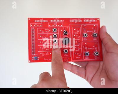 A finger points to a red electronic control circuit board for an automatic car wash system project. Stock Photo