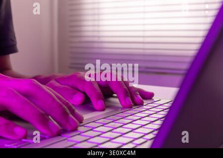 A man working on a laptop in a room with purple lighting Stock Photo