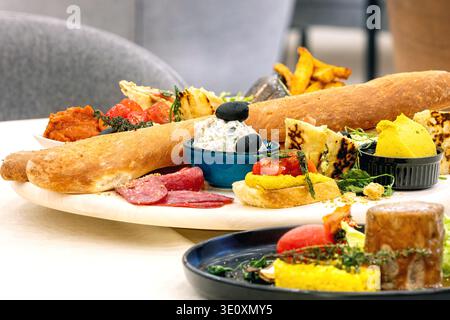 Abundant appetizer platter with baguette dips and savory snacks served on white dining table Stock Photo