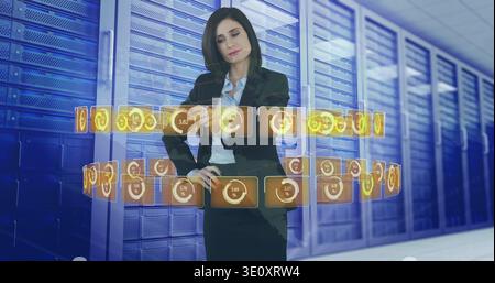 Gesturing woman in blazer manipulating holographic widgets in data center among server racks Stock Photo