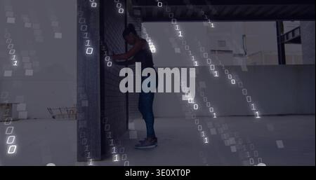 Pressing forearms on brick column, woman in activewear stretching on roof deck with binary digits Stock Photo