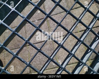 A high-contrast, diagonal composition of a dark grey metal grid or floor grate. The repeating square pattern creates a strong industrial aesthetic aga Stock Photo