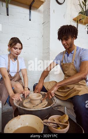 Two adults focus on crafting pottery in a cozy studio. The woman appears concentrated while the man smiles, creating a relaxed and collaborative atmos Stock Photo