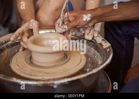Two focused adults engaged in pottery making indoors. Hands covered in clay as they skillfully shape their creations on a spinning wheel, showcasing c Stock Photo