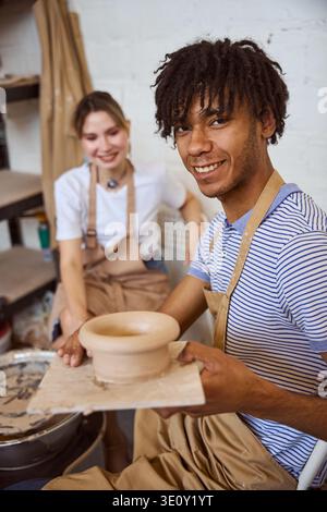 Two young adults, one African American man and one Caucasian woman, joyfully work with clay in a pottery studio. Their expressions reflect creativity Stock Photo