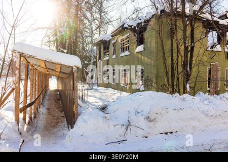 Decayed wooden house, severely damaged by fire, standing desolate in a snowy winter landscape. Broken windows, charred roof. Abandoned ruin under brig Stock Photo