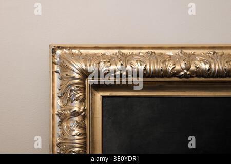 Golden picture frame corner with intricate decorative elements and artistic carving details against a gray wall background, symbolizing luxury, elegan Stock Photo