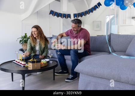 Couple sitting on gray sectional sofa at home, reaching for cupcakes on round black coffee table Stock Photo