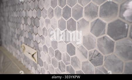 Angled close-up of gray hexagonal tiles with fresh white grout. The shallow depth of field highlights the marble texture and geometric pattern. For re Stock Photo
