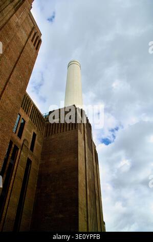 A dramatic industrial power station with a tall white chimney rises above massive brick architecture under a moody cloudy sky, conveying urban strengt Stock Photo