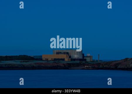 Large industrial structure of the Wylfa nuclear power station situated on the coastline at Cemaes Bay under a deep blue twilight sky Stock Photo