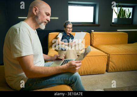 Middle-aged couple working in modern living room with laptop Stock Photo