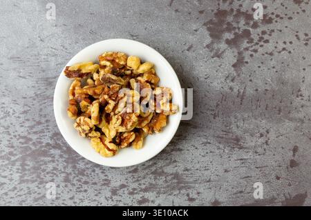 Top view of a small white bowl filled with walnuts on a gray mottled countertop. Stock Photo