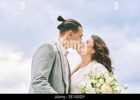 Romantic bride and groom about to kiss while holding wedding bouquet, elegant couple sharing intimate moment outdoors during joyful wedding day Stock Photo