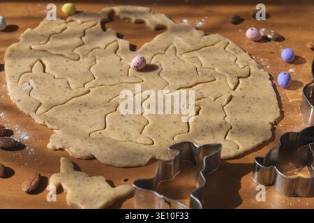 Dough with cut-out cookies in the shape of Easter bunnies, surrounded by small colorful eggs Stock Photo