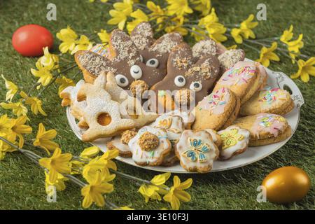 Various decorated Easter cookies on a plate next to flowers and colorful Easter eggs in the grass Stock Photo