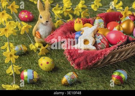 A basket full of colorful Easter eggs and a rabbit figurine with yellow flowers and chocolate eggs Stock Photo