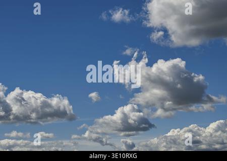 A beautiful scene of puffy white clouds against a vivid, clear blue sky, perfect for backgrounds or nature themes Stock Photo