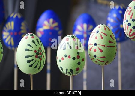 Colorful eggs with detailed patterns in vibrant green, yellow, blue and red hues mounted on sticks. Soft light highlights their festive charm, making Stock Photo