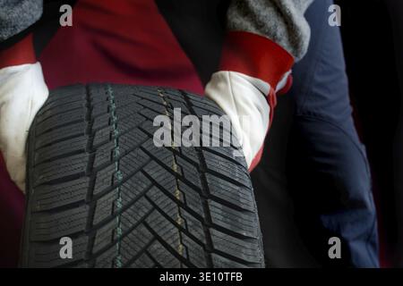 Mechanic's gloved hands inspecting a tire, highlighting tread patterns and automotive care. Depicts safety and precision in vehicle maintenance within Stock Photo