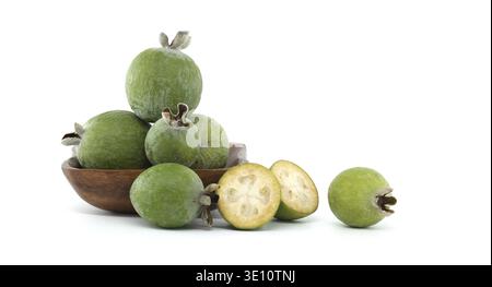 A selection of fresh feijoa fruits arranged in a wooden bowl with a few fruits sliced open, showcasing their vibrant texture and natural beauty agains Stock Photo