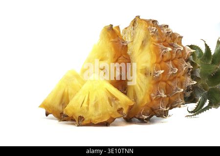 Bright yellow pineapple with green leaves, featuring fresh slices placed attractively on a white surface Stock Photo