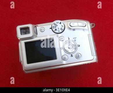 Silver digital compact camera placed on a red background, showcasing its design and features Stock Photo