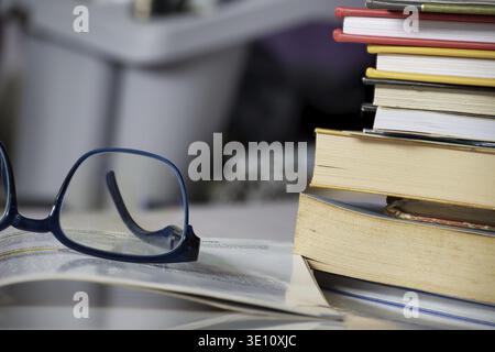 Close-up of reading glasses on open book with stack of books in study environment for learning and education concept Stock Photo