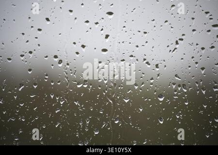 A window with raindrops on it. The raindrops are scattered all over the window, creating a blurry and hazy effect. Scene is calm and peaceful, as the Stock Photo