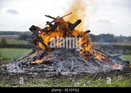 A close-up view of a bonfire with burning wood, showcasing intense flames and charred logs in an outdoor environment. It captures a warm, dramatic atm Stock Photo