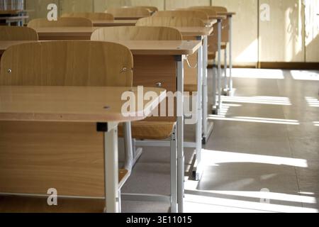 Photo of an empty classroom with wooden desks and chairs lined up in rows, sunlight streaming through the windows Stock Photo
