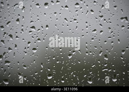 A window with raindrops on it. The raindrops are scattered all over the window, creating a blurry and hazy effect. Scene is calm and peaceful, as the Stock Photo