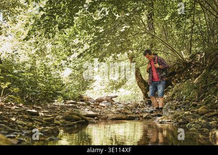 Trekking with backpack concept image. Backpacker in trekking boots crossing mountain river. Man hiking in mountains during summer trip. Vacation trip Stock Photo
