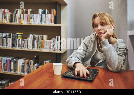 Bored student learning in university library. Young woman listening to online course from computer. Remote education. Using technology. Back to school Stock Photo