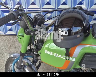 Black helmet with short visor resting on the fuel tank of a green Sis Sachs motorcycle parked against a blue tiled wall Stock Photo