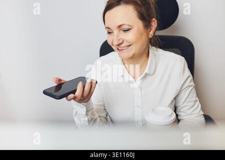 Businesswoman talking on mobile phone using speaker mode. Woman recording audio message using voice assistance and recognition function on smartphone. Stock Photo